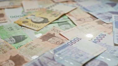 Güney Kore banknotları düz bir yüzeye dağılmış, renkli tasarımlar ve tarihsel figürlerin portreleri, çeşitli mezheplerde Güney Kore 'nin para birimini gösteriyor..