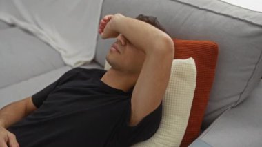 Rahat bir kanepede rahat bir şekilde dinlenen genç adam rahat bir oturma odasında yastıklar yerleştiriyor, evde rahatlık ve rahatlık hissi veriyor..