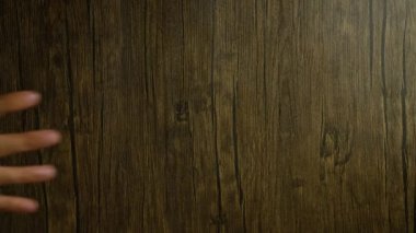 Elleri ahşap arka planda insan derisi dokusunu ve doğal ahşap yüzeyi vurgulayan hareketler gösteriyor.