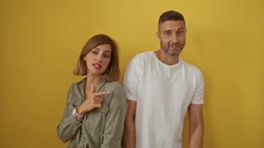 Erkek ve kadın, izole edilmiş sarı bir arkaplan karşısında şakacı bir şekilde birbirlerini gösteriyorlar ve komik ilişkilerini gösteriyorlar.