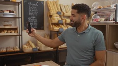 Genç İspanyol bir adam pastanede selfie çekiyor ve zafer jesti yapıyor.