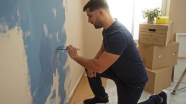 Dairesinde duvar boyayan genç adam, modern bir iç mekan ortamında taşınan kutular ve doğal ışıklarla çevrili, ev gelişimini ve iç değişimlerini vurguladı..