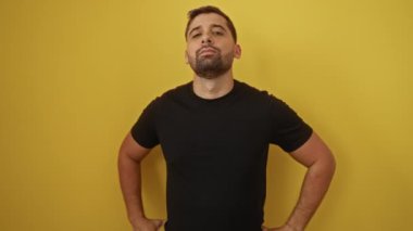 Yakışıklı görünümünü vurgulayan parlak sarı bir arkaplana karşı kollarını açarak güvenle poz veren genç adam