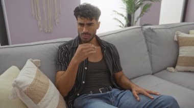 Oturma odasında sakallı genç adam rahat yastıklarla ve ev bitkileriyle çevrili rahat koltukta otururken kötü kokudan burnunu çimdikliyor..