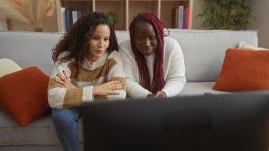 Oturma odasındaki kanepede birlikte televizyon seyreden kadın arkadaşlar etrafı dekorasyon kitaplarıyla çevrili rahat evlerinde rahatlıyor gülümsüyor ve kaliteli vakit geçiriyorlar..