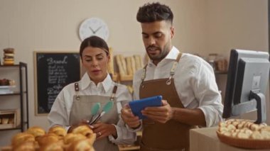 Pastanede çalışan bir adam ve bir kadın tezgahın üzerinde hamur işleri ve önlük giymiş bir tabletle kapalı bir dükkânda iş konuşuyorlar..
