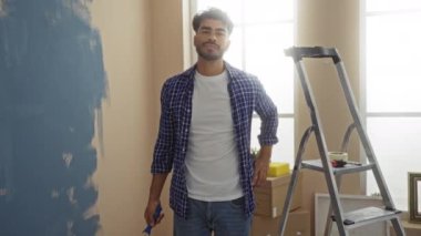 Ev yenileme projesi sırasında yeni dairede mavi boya silindirli genç bir adam oturma odasını boyuyor.