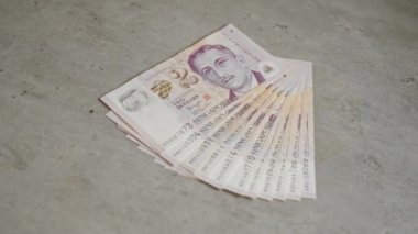 Singapur doları banknotları sert bir beton yüzeye yayılarak finansal temaları net ve ayrıntılı para birimi yakın çekimleri ile vurguluyor.