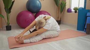 Beyazlı olgun bir kadın spor salonunda yoga minderi üzerinde renkli egzersiz topları ve bitkilerle bir chihuahua köpeğiyle egzersiz yapıyor.