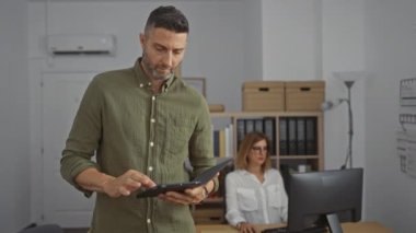 Kadın modern ofis ortamında bilgisayar üzerinde çalışırken erkek tablet kullanıyor, profesyonel işbirliği ve üretkenlik sergiliyor.