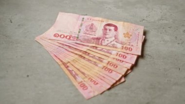 Tayland baht banknotları yığını beton bir yüzeye serilmiş, canlı renkleri ve para biriminin karmaşık detaylarını gözler önüne seriyor..