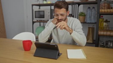 Ofiste çalışan yakışıklı İspanyol bir adam çevrimiçi görevler için tablet kullanıyor, arka planda rafları olan modern bir iç mekan ile profesyonel bir atmosfer yaratıyor.