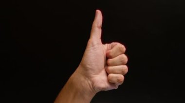Adam sağlam bir siyah arkaplan karşısında el hareketi yapıyor. Onay ve pozitiflik taşıyor.