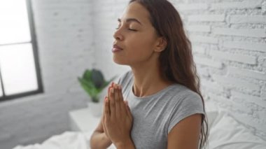 Minimalist bir yatak odasında sakince meditasyon yapan bir kadın huzurlu bir ifadeyle sükunet ve farkındalık sergiliyor.