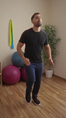 Spor salonunda egzersiz yapan, arka planda spor topları olan, günlük spor giysileri giyen, sağlıklı yaşam tarzını ve iç mekandaki fitness rutinini gösteren bir adam..