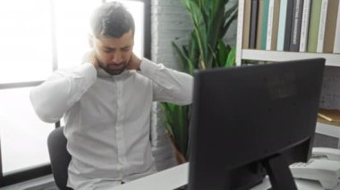 Ofis masasında boyun ağrısı çeken bir adam, iş ortamında rahatsızlığını gösterir. Modern iç mekan, profesyonel ortamdaki stres ve yorgunluğu yansıtır..