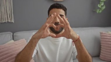 İnsan, evinde elleriyle kalp şekli oluşturur. Modern oturma odasında otururken sevgi ve neşe gösterir..