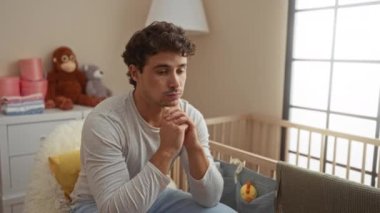 Genç adam düşünceli bir şekilde rahat bir yatak odasında, yumuşak ışıkla çevrili, huzurlu bir ev ortamında sıcak ve düşünceli bir atmosfer yaratıyor..