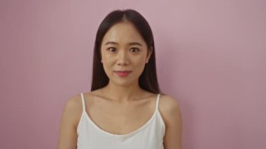 Çekici genç Çinli kadın pembe arka planda, gülümserken kameraya bir öpücük yolluyor, büyüleyici ve eğlenceli bir anı yakalıyor..