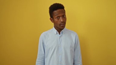 Afro-Amerikan gömlekli genç adam, kuşkucu bir duruş içinde, alaycı açık ağızlı, izole sarı arka plana karşı