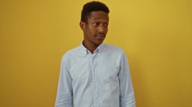 Genç Afro-Amerikalı bir adam tişört giyiyor, eli ağızında duruyor, sarı arka planda gizli fısıldaşmalar anlatıyor.