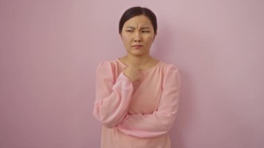 Soyutlanmış pembe arka planda duran genç Çinli kadın, sinirsel gerginlik stresi, ısıran eller ve sorunlara bakan