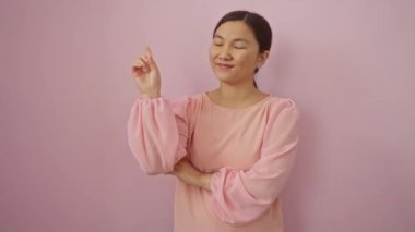 Genç Çinli kadın mutlu bir şekilde ayakta duruyor ve gülümsüyor. Parmağıyla soyutlanmış pembe bir arka planı işaret ediyor.