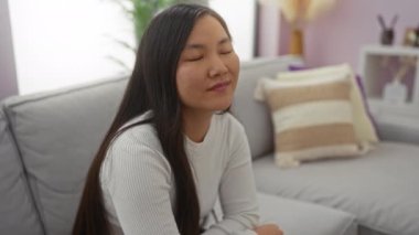 Oturma odasındaki rahat koltukta, yumuşak yastıklı ve ev dekorlu bir kadın, evinde huzurlu bir anın tadını çıkarıyor..