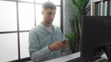 Ofiste genç bir adam, akıllı bir telefonla mesajları kontrol ediyor. Masada öylesine poz veriyor. Etrafı modern, havadar bir iç mekan ve yeşillikle çevrili..