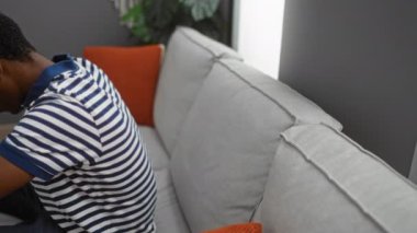 Genç adam rahat bir kanepede rahat bir oturma odasında çizgili gömlek ve renkli yastıklarla dinleniyor..