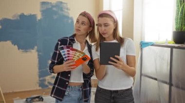 Oturma odasında dijital tablet ve renk paletiyle resim yapmayı seçen kadın kardeşler..