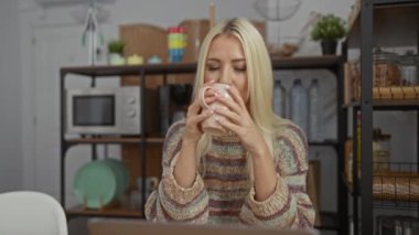 Kadın rahat bir oturma odasında dizüstü bilgisayarla çalışırken kahveden zevk alıyor. Modern dekor ve pencereden gelen doğal ışık rahatlamış bir ev atmosferi sergiliyor..