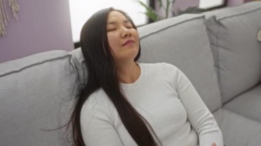 Modern bir evde, rahat bir kanepede dinlenen bir kadın, huzur ve huzur dolu bir oturma odasında kuruluyor..