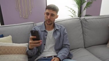 Oturma odasında elinde telefonla selfie çeken bir adam rahat bir ev atmosferi için rahat dekor ve doğal ışıklandırmayla modern kapalı mekan dekorunu sergiliyor..