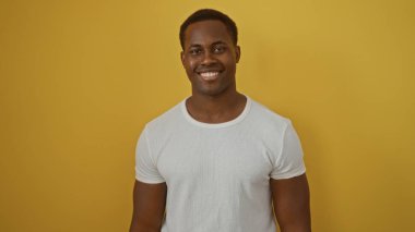 Parlak sarı arka plana gülümseyen genç adam, izole edilmiş, özgüven, mutluluk ve modern tarz sergiliyor..