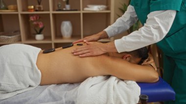 Sağlık merkezindeki terapist sıcak taş masajı yaptırıyor.