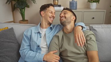 Sevgi dolu çift oturma odasındaki kanepelerinde neşeli bir anı paylaşıyor. Eşcinsel aşkını, aile bağını ve evlerinin sıcak atmosferini yansıtıyorlar..