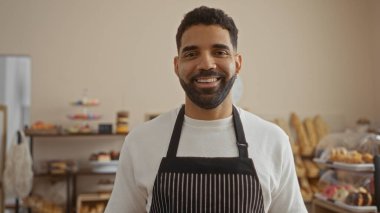 Pasta ve ekmekle çevrili çizgili bir önlükle bir pastanede gülümseyen İspanyol genç adam..