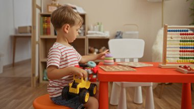 Sarışın çocuk evde rahat bir anaokulunda oyuncaklarla ve bulmacalarla oynuyor.