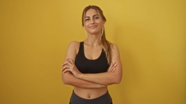Güvenle gülümseyen bir kadın, kolları bağlı, parlak sarı arka plan, pozitifliği ve güçlenmeyi simgeliyor.
