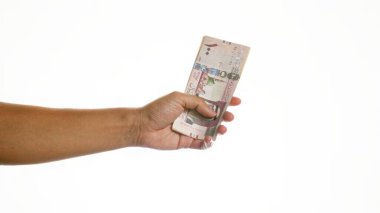 Suudi Arabistan riyal notlarını beyaz bir arkaplana karşı tutan bir elin yakınlaştırılması, minimalist ve izole bir ortamda mali işlem veya ödeme kavramını vurguluyor