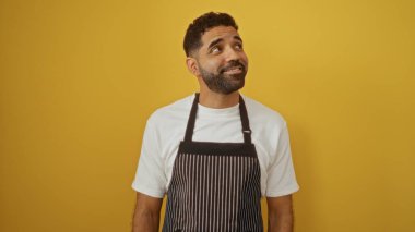 Çizgili önlüklü genç adam, izole edilmiş sarı bir arka plana doğru bakıyor. Çekici ve neşeli bir hava veriyor..