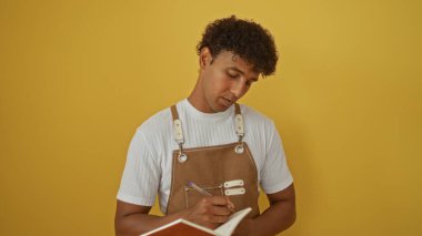 İzole edilmiş sarı bir arkaplanda duran genç İspanyol adam notlar yazıyor.