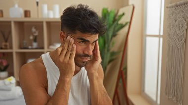 Kaplıca odasında yakışıklı genç bir adam aynaya bakarken yüzünü düzeltiyor. Etrafı bitkiler ve yumuşak ışıklandırmalarla dolu.