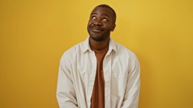 Yakışıklı, Afro-Amerikalı bir adam, parlak sarı bir duvara gülümsüyor. Çekici, izole bir arka plan yaratıyor.