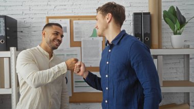 Ofisteki yakışıklı adamlar, reklam panosu ve rafların yer aldığı modern bir iş yeri ortamının ortasında dostça yumruklarını şişiriyorlar.