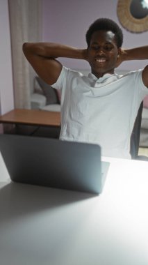 Oturma odasında dizüstü bilgisayarı olan genç bir adam gülümsüyor ve içeride eğleniyor.