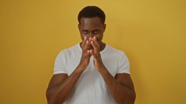 İzole edilmiş sarı arka plana karşı duran genç adam, kendine güvenen bir ifadeyle, günlük beyaz gömlek giyiyor ve odaklanma ve kararlılık gösteriyor..