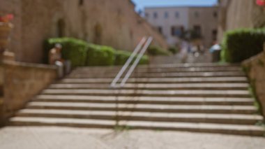 Açık mavi gökyüzü altında büyük taş basamaklar, yeşil çitler ve tarihi mimarinin yer aldığı Mallorca 'da bulanık bir manzara.