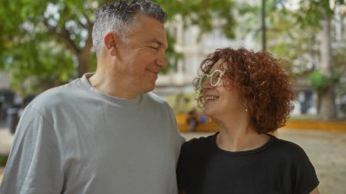Güneşli bir günde orta yaşlı bir çift, şehir parkında neşeli bir anı paylaşıyor, açık havada gülümsüyor, aşkı ve bağlantıyı canlandırıyor.